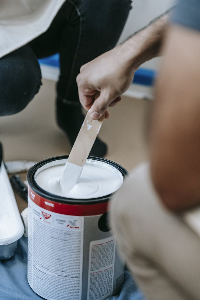 Close-up of a person mixing white paint in a can, preparing for home renovation.